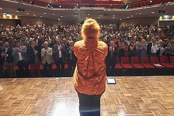 Margit Hertlein von hinten auf der Bühne vor großem Publikum in Villach