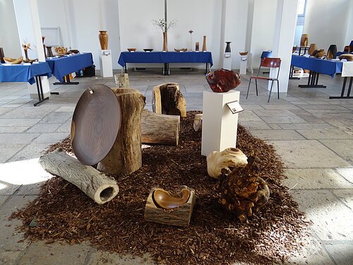 Auf dem Boden ist Rindenmulch verstreut, daraufsind diese einzele Holzstücke ausgestellt. der Untergrubn bietet einen super platz und lässt die Einzelstpcke unter dem Lichteinfall, super zur Geltung kommen.
