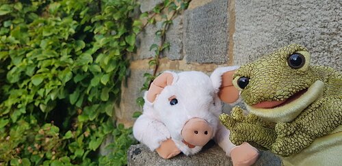 Ein Flüschschwein und ein Plüschfrosch sitzen auf einer mit Efeu bewachsenen Mauer.