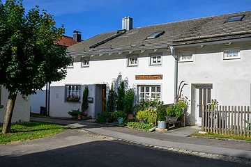 Ein Jurahaus in Suffersheim, das Wollstüberl. vor dem Haus befinden sich einige Stäucher, Die Tür und die Fenster sind mit einem hellgrauen Farbanstrich abgesetzt