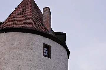 Runder weißer Turm mit roten Dachziegeln, zwei kleinen Fenstern und Laterne an der Wand bei Dämmerung.